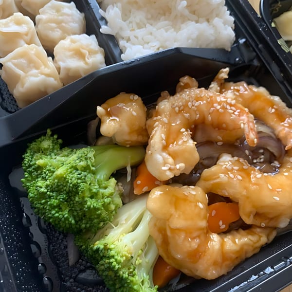 A Big Bang Sushi & Poke bento box with shrimp, broccoli, rice, and dumplings.